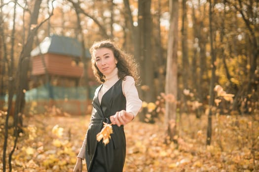 Attractive young woman walking in autumn park, happy mood and fashion style trend and curly long brown hair. Fall season and pretty female portrait. Millennial generation