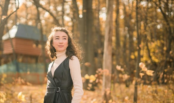 Attractive young woman walking in autumn park, happy mood and fashion style trend and curly long brown hair. Fall season and pretty female portrait. Millennial generation