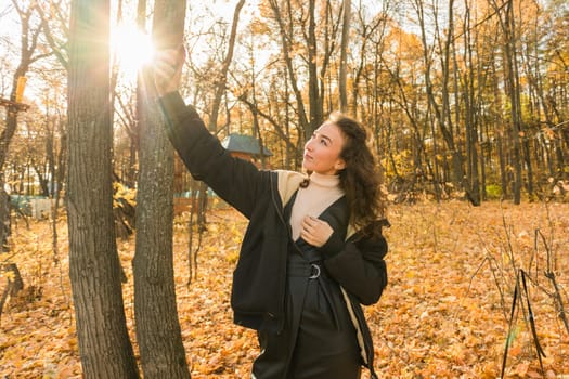 Attractive young woman walking in autumn park, happy mood and fashion style trend and curly long brown hair. Fall season and pretty female portrait. Millennial generation