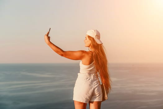 Selfie woman sea. The picture depicts a woman in a cap and tank top, taking a selfie shot with her mobile phone, showcasing her happy and carefree vacation mood against the beautiful sea backgroun.