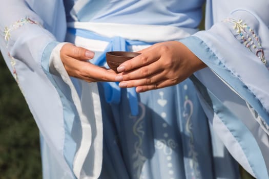 A woman in a traditional Chinese hanfu dress holds a cup with a drink close-up