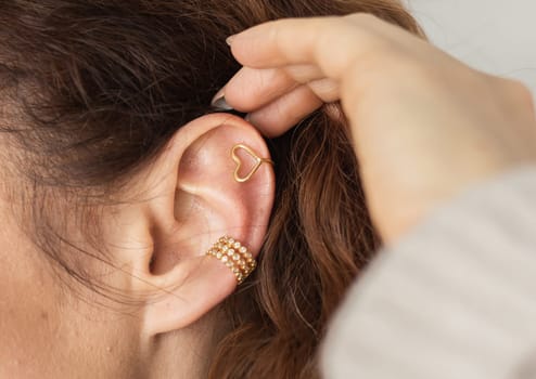 Cropped close-up shot of a young woman with two asymmetrical golden ear cuffs. Female with golden ear cuffs, side view