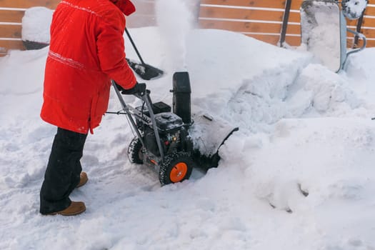 A man clear snow from backyard with snow blower. Winter season and snow blower equipment.