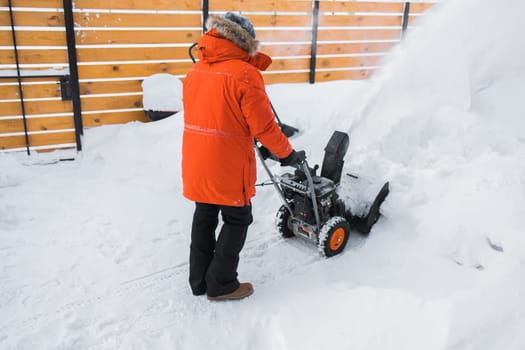 A man clear snow from backyard with snow blower. Winter season and snow blower equipment.