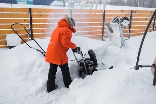 A man clear snow from backyard with snow blower. Winter season and snow blower equipment.