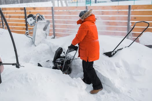 A man clear snow from backyard with snow blower. Winter season and snow blower equipment.