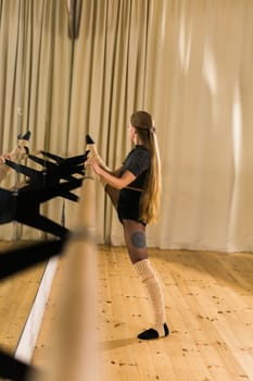 Young woman ballerina stretching and training at barre in dance studio - ballet and dancer
