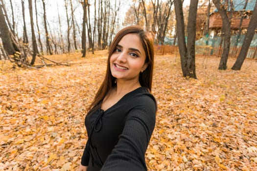 Close-up portrait of a young beautiful confident Indian Asian woman in fall outdoor. Happy and natural smiling female. Generation z and gen z youth