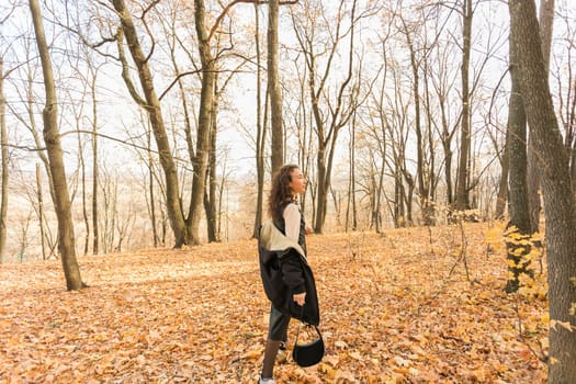 Attractive young woman walking in autumn park, happy mood and fashion style trend and curly long brown hair. Fall season and pretty female portrait. Millennial generation