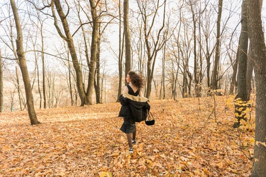 Attractive young woman walking in autumn park, happy mood and fashion style trend and curly long brown hair. Fall season and pretty female portrait. Millennial generation