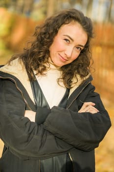 Attractive young woman walking in autumn park, happy mood and fashion style trend and curly long brown hair. Fall season and pretty female portrait. Millennial generation