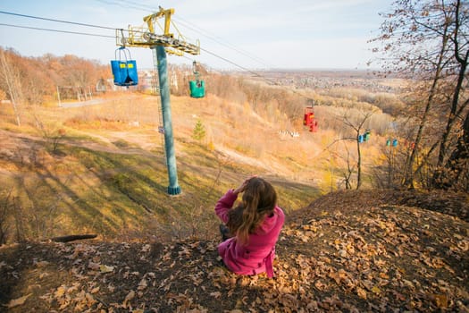 Back view of a girl woman resting on autumn park in fall season and look at the cable car. Generation Z and gen z youth. Copy empty space for text