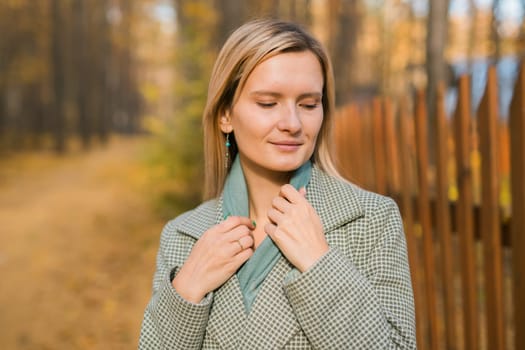 Blonde woman in elegant gray coat walks in the sunny autumn season park. Generation z and gen z youth concept