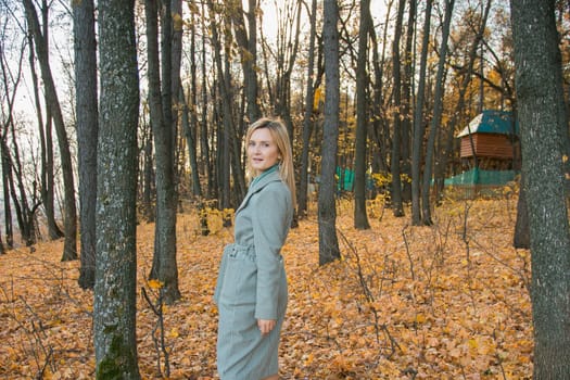 Blonde woman in elegant gray coat walks in the sunny autumn season park. Generation z and gen z youth concept