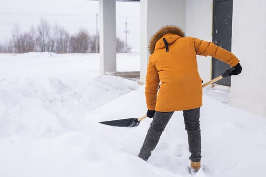 Young man clearing snow in his backyard village house with shovel. Remove snow from the sidewalk