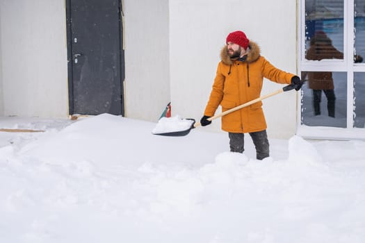 A man cleans and clears the snow in front of the house on frosty day. Cleaning the street from snow on a winter day. Snowfall and severe snowstorm in winter