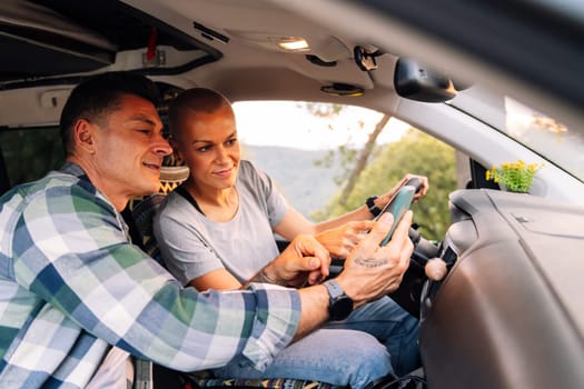 couple planning on the mobile phone the route through the countryside in their camper van, concept of couple adventure travel and active tourism in nature