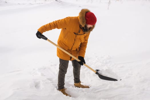 Young man clearing snow in his backyard village house with shovel. Remove snow from the sidewalk