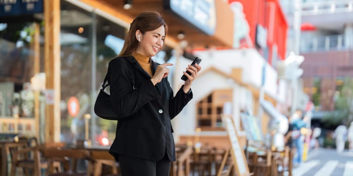 Asian professional businesswoman holding cellphone using smartphone standing or walking on big city urban street outside. Successful Asian business woman.