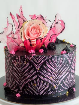 frosted icing black decorate cake for birthday celebration, real rose topping and pink sweet swirls studio isolated shot