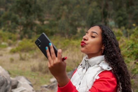 latin american vlogger girl sends a kiss to her followers during a live show on a mountain. High quality photo