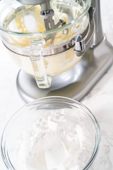 Whisking buttercream frosting in a glass mixing bowl with an electric kitchen mixer for American flag mini cupcakes.