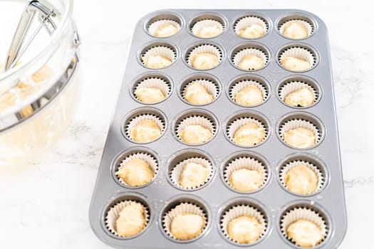 Scooping cupcake batter with dough scoop into a baking pan with liners to bake American flag mini cupcakes.