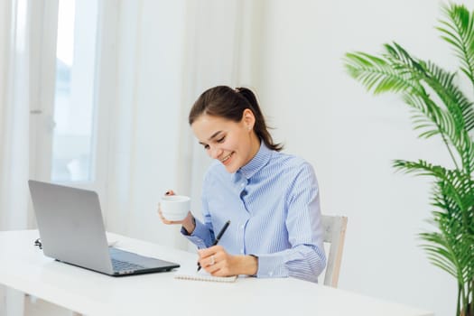 Image of young pleased happy cheerful cute beautiful business woman sit indoors in office using laptop computer listening music with earphones.