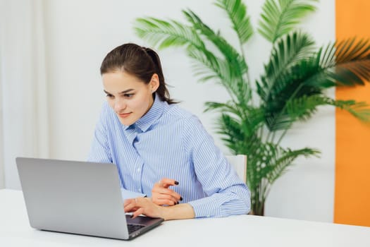 Image of young pleased happy cheerful cute beautiful business woman sit indoors in office using laptop computer listening music with earphones.