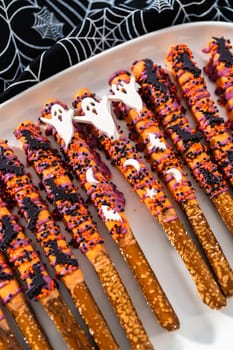 Halloween chocolate-covered pretzel rods with sprinkles on a white serving plate.