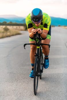 Triathlete riding his bicycle during sunset, preparing for a marathon. The warm colors of the sky provide a beautiful backdrop for his determined and focused effort