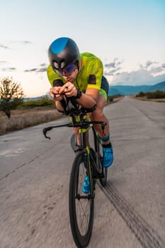 Triathlete riding his bicycle during sunset, preparing for a marathon. The warm colors of the sky provide a beautiful backdrop for his determined and focused effort