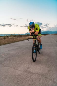 Triathlete riding his bicycle during sunset, preparing for a marathon. The warm colors of the sky provide a beautiful backdrop for his determined and focused effort