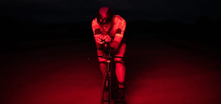 A triathlete rides his bike in the darkness of night, pushing himself to prepare for a marathon. The contrast between the darkness and the light of his bike creates a sense of drama and highlights the athlete's determination and perseverance