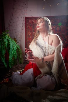 Beautiful European girl looking like Arab woman in red room with rich fabrics and carpets in sultan harem. Photo shoot of an oriental style odalisque. A model poses in sari as indian woman in india