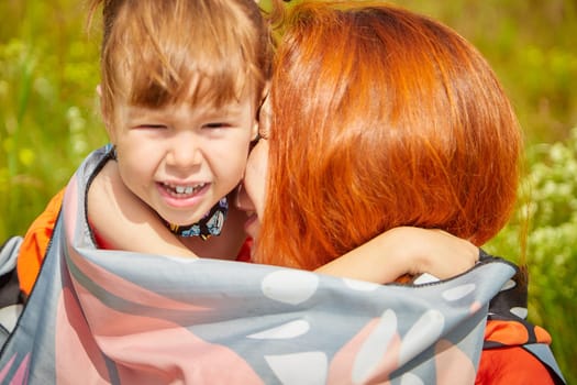 Happy female family with mother and daughter on green and yellow meadow full of grass and flower. Woman with red hair and blonde girl having fun, joy and hug in sunny summer day. Concept family love