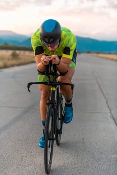 Triathlete riding his bicycle during sunset, preparing for a marathon. The warm colors of the sky provide a beautiful backdrop for his determined and focused effort