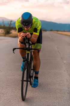 Triathlete riding his bicycle during sunset, preparing for a marathon. The warm colors of the sky provide a beautiful backdrop for his determined and focused effort