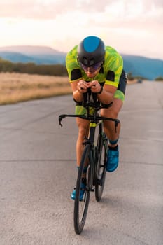 Triathlete riding his bicycle during sunset, preparing for a marathon. The warm colors of the sky provide a beautiful backdrop for his determined and focused effort