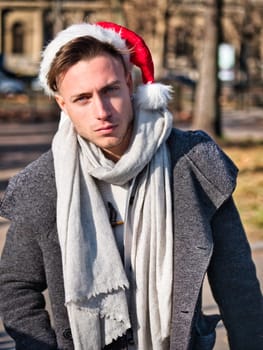 Young guy in scarf and Santa hat looking at camera on blurred background of street on Christmas day
