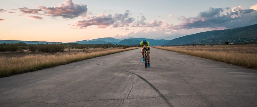 Triathlete riding his bicycle during sunset, preparing for a marathon. The warm colors of the sky provide a beautiful backdrop for his determined and focused effort