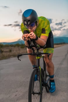 Triathlete riding his bicycle during sunset, preparing for a marathon. The warm colors of the sky provide a beautiful backdrop for his determined and focused effort