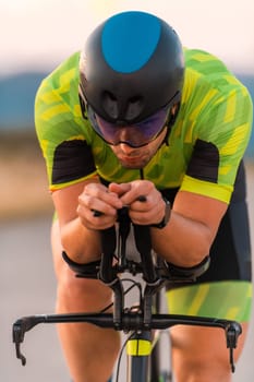 Close up photo of triathlete riding his bicycle during sunset, preparing for a marathon. The warm colors of the sky provide a beautiful backdrop for his determined and focused effort