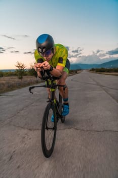 Triathlete riding his bicycle during sunset, preparing for a marathon. The warm colors of the sky provide a beautiful backdrop for his determined and focused effort