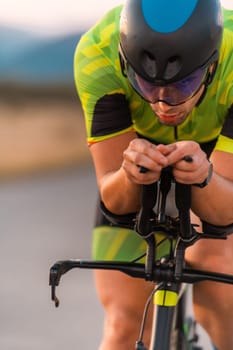 Close up photo of triathlete riding his bicycle during sunset, preparing for a marathon. The warm colors of the sky provide a beautiful backdrop for his determined and focused effort