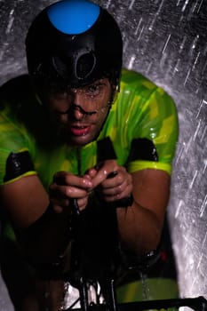 A triathlete braving the rain as he cycles through the night, preparing himself for the upcoming marathon. The blurred raindrops in the foreground and the dark, moody atmosphere in the background add to the sense of determination and grit shown by the athlete