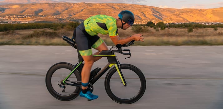 Triathlete riding his bicycle during sunset, preparing for a marathon. The warm colors of the sky provide a beautiful backdrop for his determined and focused effort