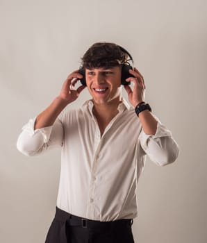 A young handsome man in a white shirt is listening to music on headphones, in studio shot