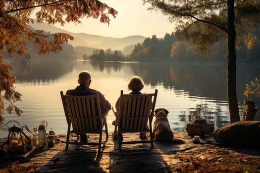 An elderly couple sits in armchairs on the shore of a lake with a dog. Camping, recreation.