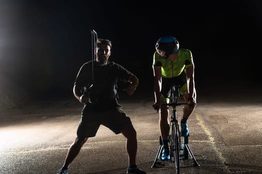 Behind the scenes. Professional videographer on a night shoot with a triathlete riding a bicycle for video recording purposes.